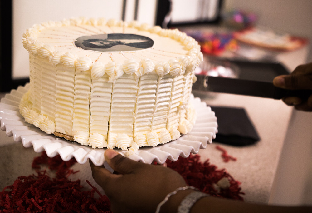 Photo of a birthday cake being cut. The birthday cake has a small image of Frederick Douglass on top. 